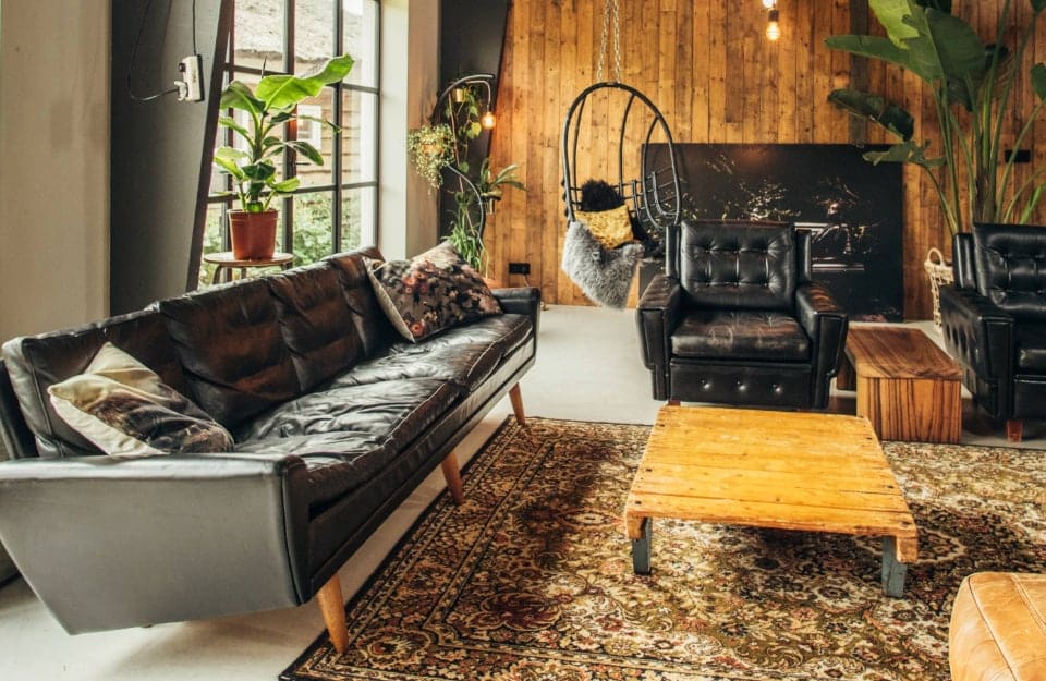 Parte di un luminoso e grande salotto con arredi di recupero e sedute in stile modernista Mid-Century come un grande divano in pelle nera e, dello stesso materiale, una poltrona nera