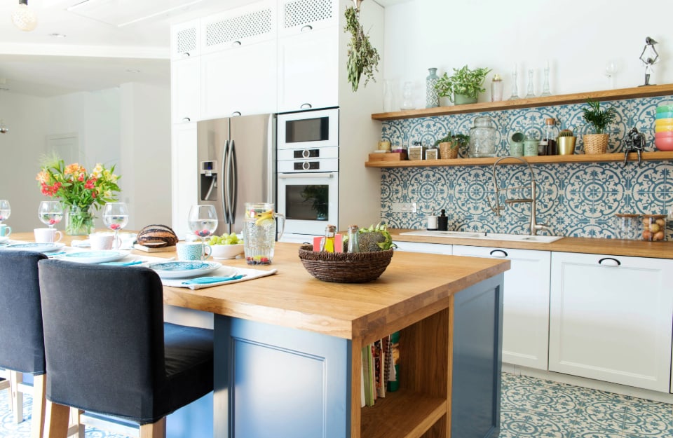 Cucina in stile mediterraneo, con paraschizzi in maiolica e isola centrale con sgabelli, il tutto nei colori del bianco, dell'azzurro e del legno naturale