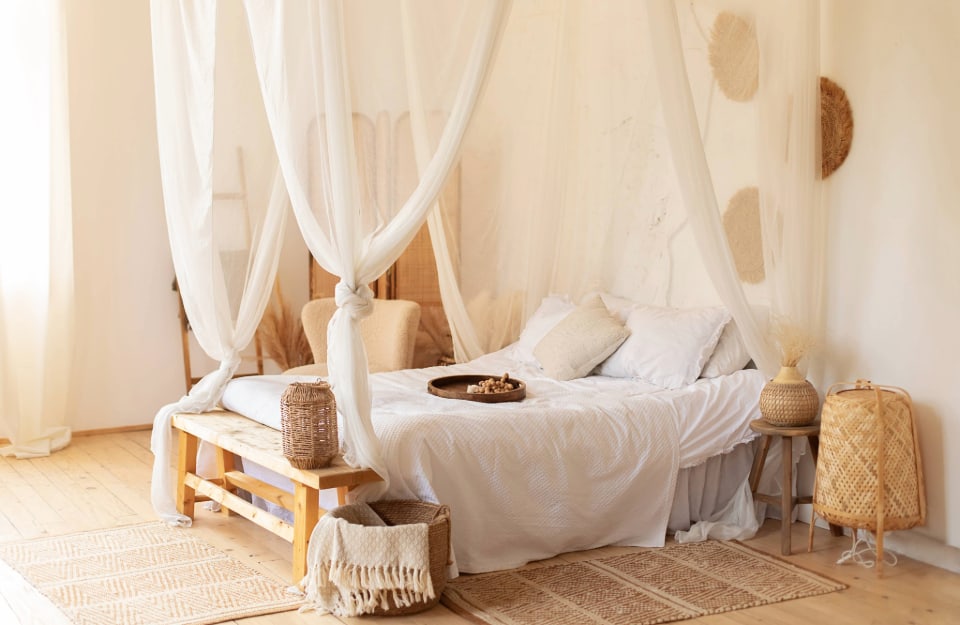Una camera da letto in stile mérida, con baldacchino, letto in legno sobrio, lenzuola in cotone, elementi in vimini, tappeti tipo stuoia e decorazioni tradizionali alle pareti color beige