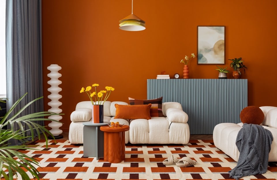 Soggiorno rétro contemporaneo con parete arancione, divani bouclé e tappeto geometrico
