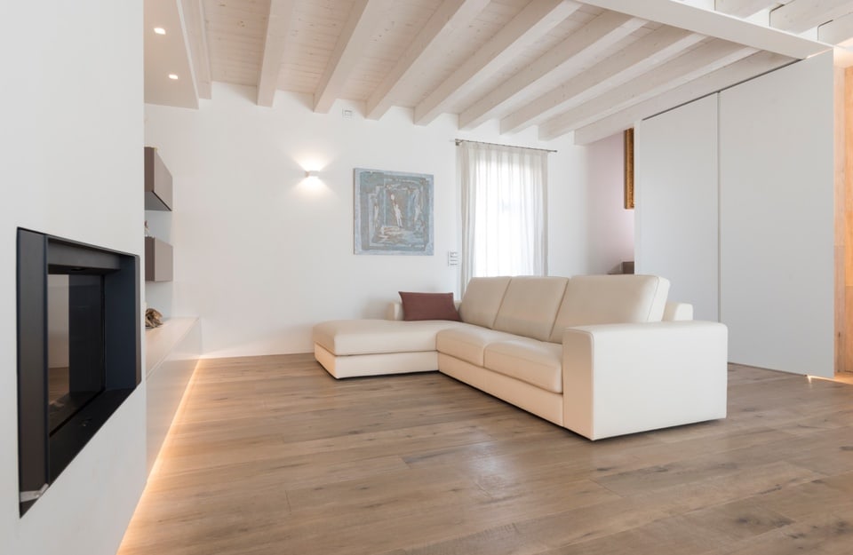 Soggiorno minimal con divano chiaro, parquet e camino moderno